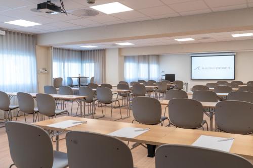 a room with tables and chairs and a projection screen at Maritim Fjordhotel in Flekkefjord
