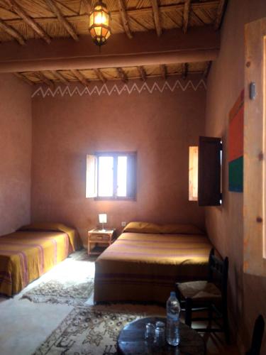 a bedroom with two beds and a table and a window at Dar Bilal in Aït Ben Haddou
