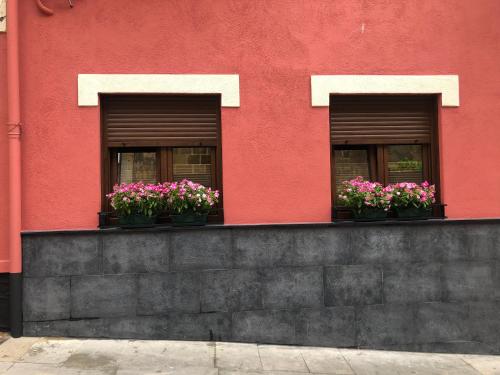 two windows with flowers on a red building at KALA apartamentua Parking gratuito cercano in Bermeo