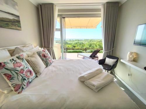 a bedroom with a white bed with a large window at Sara's Upmarket Apartment - Lagoon Views, Patio, Braai & WIFI & DSTV in Plettenberg Bay