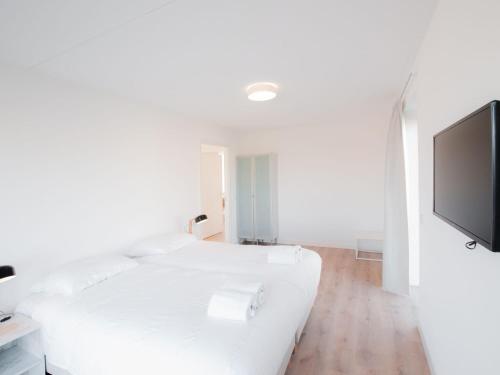 Habitación blanca con cama y TV de pantalla plana. en Modern wellness lodge with sunshower in a national park, en Tholen