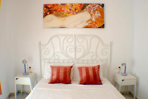 Una cama blanca con almohadas rojas y una pintura en la pared. en La Pimentera Centro Histórico - Marbella, en Marbella