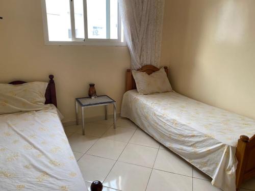 a bedroom with two beds and a table with a window at Appartement agadir in Agadir