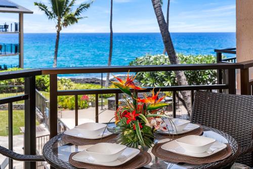 a table with plates and flowers on a balcony with the ocean at Kona Makai 6204 in Kailua-Kona