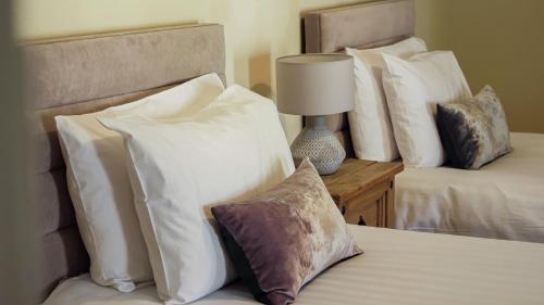 a bedroom with two beds with white pillows and a lamp at Denvir's of Downpatrick in Downpatrick