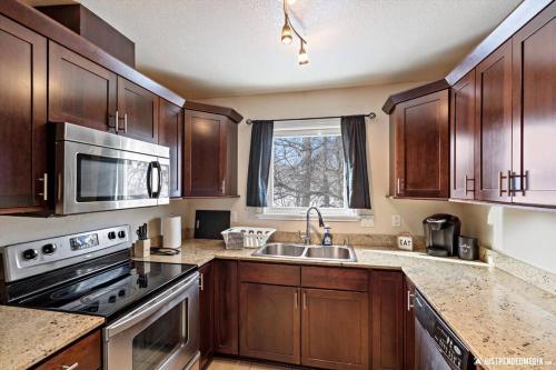 a kitchen with wooden cabinets and a sink and a microwave at Alaska Townhouse Getaway: Anchorage Cozy Retreat - Close to Downtown in Anchorage
