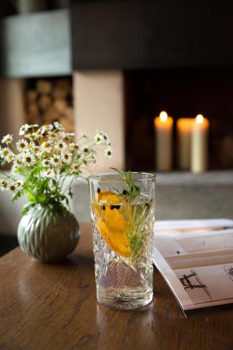 a glass of water with an orange and a vase of flowers at Familienhotel Mateera Gargellen / Montafon in Gargellen