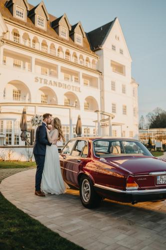 a bride and groom standing next to a car at Strandhotel Glücksburg in Glücksburg