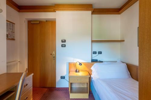 a bedroom with a bed and a desk with a lamp at Hotel Meida in Pozza di Fassa