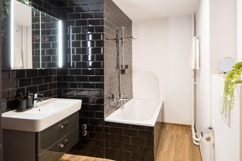 a black tiled bathroom with a sink and a bath tub at Marché 28 Guesthouse in Montreux