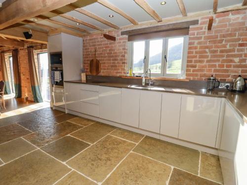 una cocina con armarios blancos y una pared de ladrillo en The Stables en Ledbury