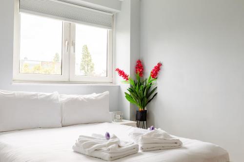 1 dormitorio con 1 cama blanca y un jarrón de flores rojas en Cosy 3 Bed Flat Ideal for Trips to London en Londres