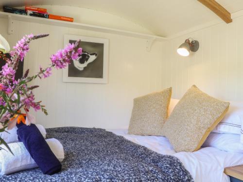 sypialnia z łóżkiem z poduszkami i wazonem z kwiatami w obiekcie Bosulla Shepherds Hut w mieście Penzance