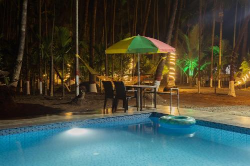 a swimming pool with a table and a green umbrella at Coco Palms Inn in Alibaug