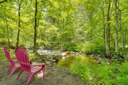 two red chairs sitting next to a stream at A-Frame Log Home with Game Room Near Lake George! in Bolton