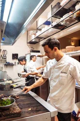 three men in a kitchen preparing food on a grill at Puerta del Cielo Hotel Origen in Bacalar