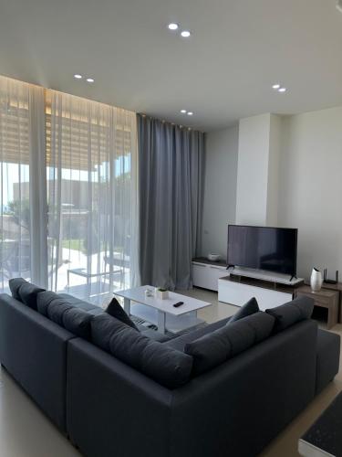 a living room with a black couch and a tv at Green Coast Resort Vila 143B in Dhërmi