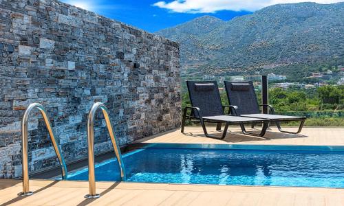 twee stoelen en een tafel naast een zwembad bij Aelia Suites in Agios Nikolaos