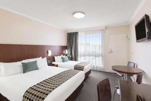 a hotel room with two beds and a table and a tv at BreakFree Queanbeyan in Queanbeyan