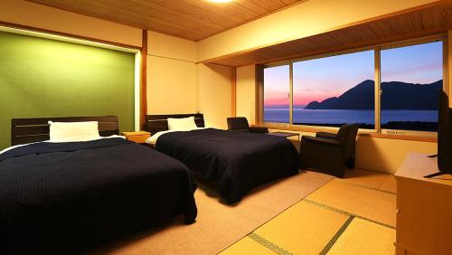 a room with two beds and a large window at Okukinosaki Seaside Hotel in Toyooka