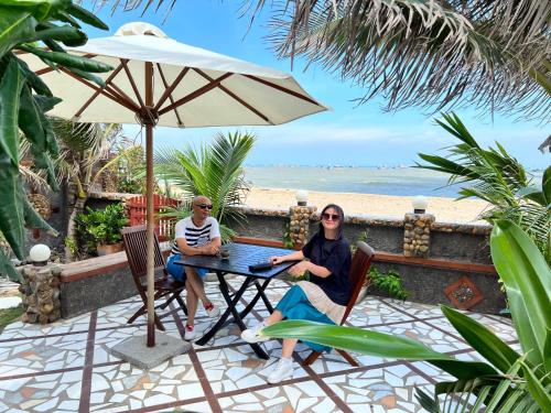 two people sitting at a table under an umbrella on the beach at Sầm Sơn Boutique Hotel Phan Thiết in Phan Thiet