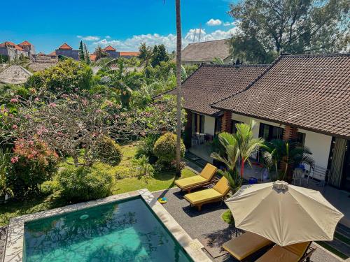 a pool with an umbrella and chairs and a house at Lemon Guest House in Canggu