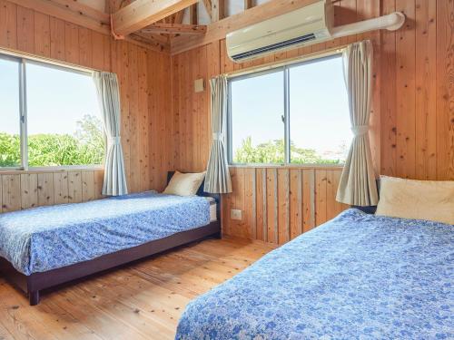 2 Betten in einem Zimmer mit Holzwänden und Fenstern in der Unterkunft Pension Snadun in Ginoza