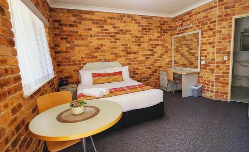 a bedroom with a bed and a table and a brick wall at Golf Club Motor Inn Wingham in Wingham