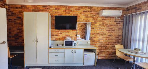 a kitchen with a white cabinet and a tv on a brick wall at Golf Club Motor Inn Wingham in Wingham