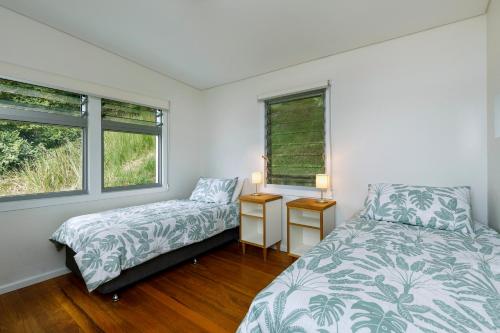 1 dormitorio con 2 camas y 2 ventanas en Currawong Beach Cottages, en Great Mackerel Beach