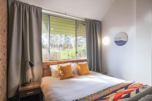 a bedroom with a bed with orange pillows and a window at Alpine Gables 11 2 Clyde Street in Jindabyne