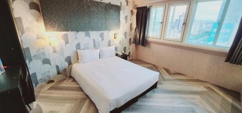 ein kleines Schlafzimmer mit einem weißen Bett in einem Zimmer mit Fenstern in der Unterkunft Gugis Inn in Taipeh