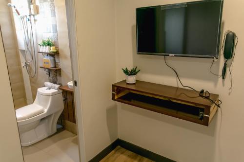 a bathroom with a toilet and a television on a wall at Midway Stay Apartments Dumaguete in Dumaguete