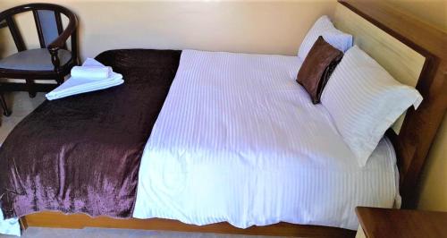 um quarto com uma cama com lençóis brancos e uma cadeira em Wayu Nova Guesthouse em Bulbula