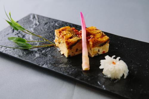a black plate with a piece of sushi and rice at Suisui Garden Ryokan (in the Art Hotel Kokura New Tagawa) in Kitakyushu