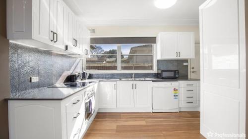 a white kitchen with white cabinets and a window at Costa Park Cottage Ena in Armidale