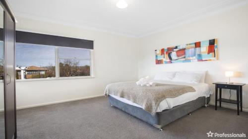 a white bedroom with a bed and a window at Costa Park Cottage Ena in Armidale