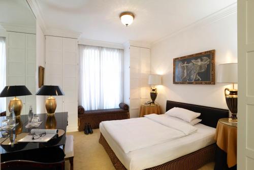 a bedroom with a white bed and a desk and a window at Hotel Opera in Munich