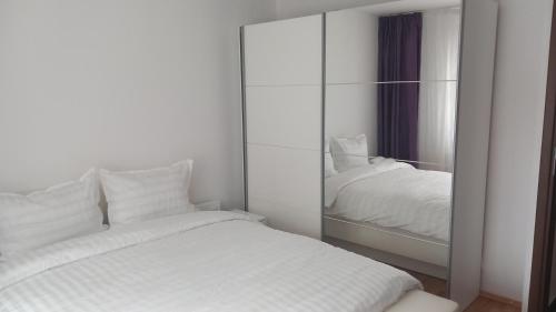 Schlafzimmer mit einem weißen Bett und einem Spiegel in der Unterkunft Apartament Brasov in Braşov