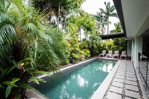 una piscina con palmeras y una casa en Chez Brolga, en Port Douglas
