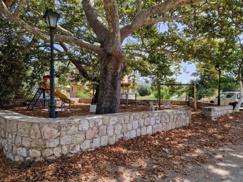 a stone wall with a tree and a playground at MemRo Village House in Atsoupádhes
