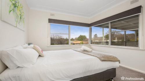 a white bedroom with a large window and a bed at Costa Park Cottage Dio in Armidale