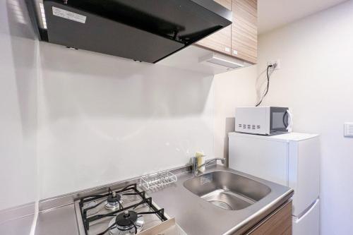 una pequeña cocina con fregadero y microondas en Lafesta Higashikomagata, en Tokio