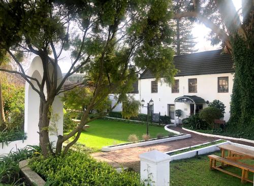 a white house with a tree and a bench at Houw Hoek Hotel in Botrivier