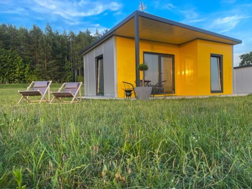 a small yellow house with two chairs in a field at Domki Nad Malowniczym Stawem / Raj Dla Wędkarzy / Mazury in Piecki