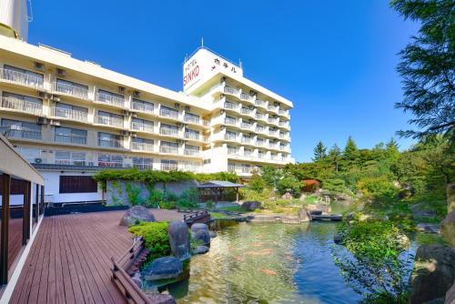 a hotel with a pond in front of a building at Ooedo Onsen Monogatari Hotel Shinko in Fuefuki