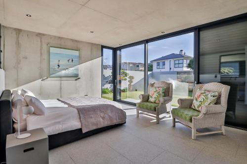 a bedroom with a bed and two chairs and windows at Mi Amor Myoli Beach in Sedgefield