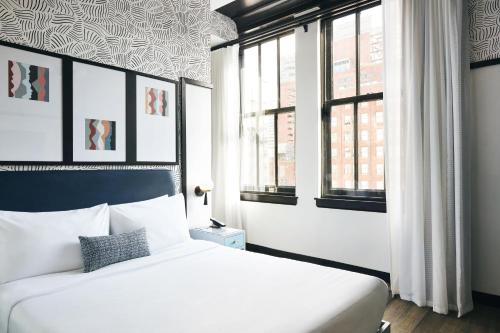 a bedroom with a white bed and two windows at Kinley Cincinnati Downtown, a Tribute Portfolio Hotel in Cincinnati