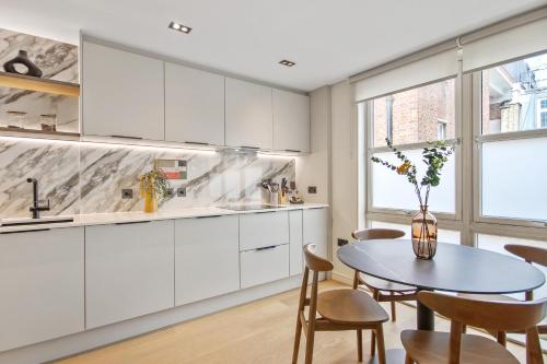 a kitchen with white cabinets and a table and chairs at Bow Lane by Aeria Apartments in London