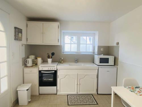 une cuisine avec des armoires blanches, un évier et un micro-ondes dans l'établissement Appartement cosy, jardin privé, 100m de la plage, Côte de Granit Rose - FR-1-542-10, à Trégastel